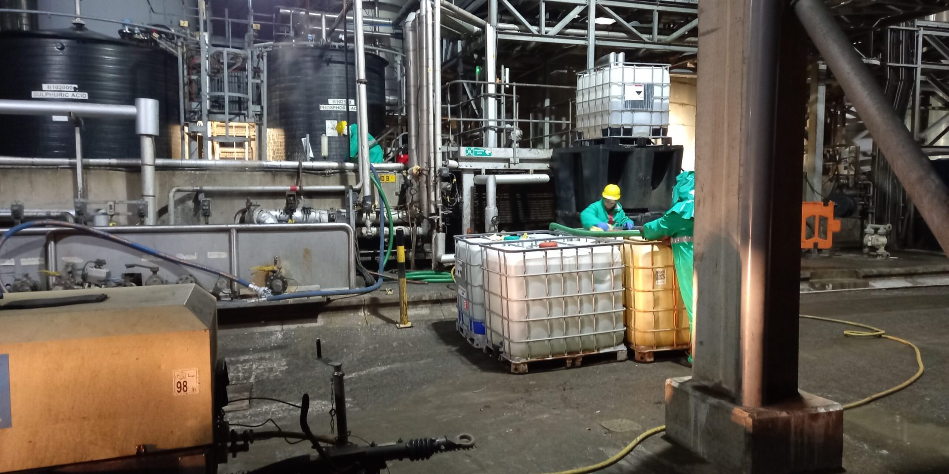 Two workers filling up four large containers of liquid